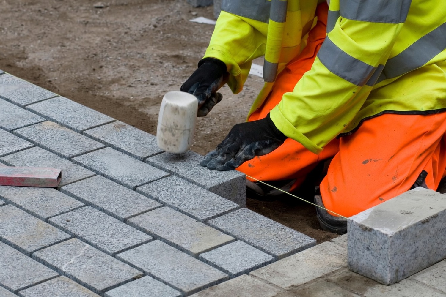 Operative tapping a paver into bedding sand with a rubber mallet