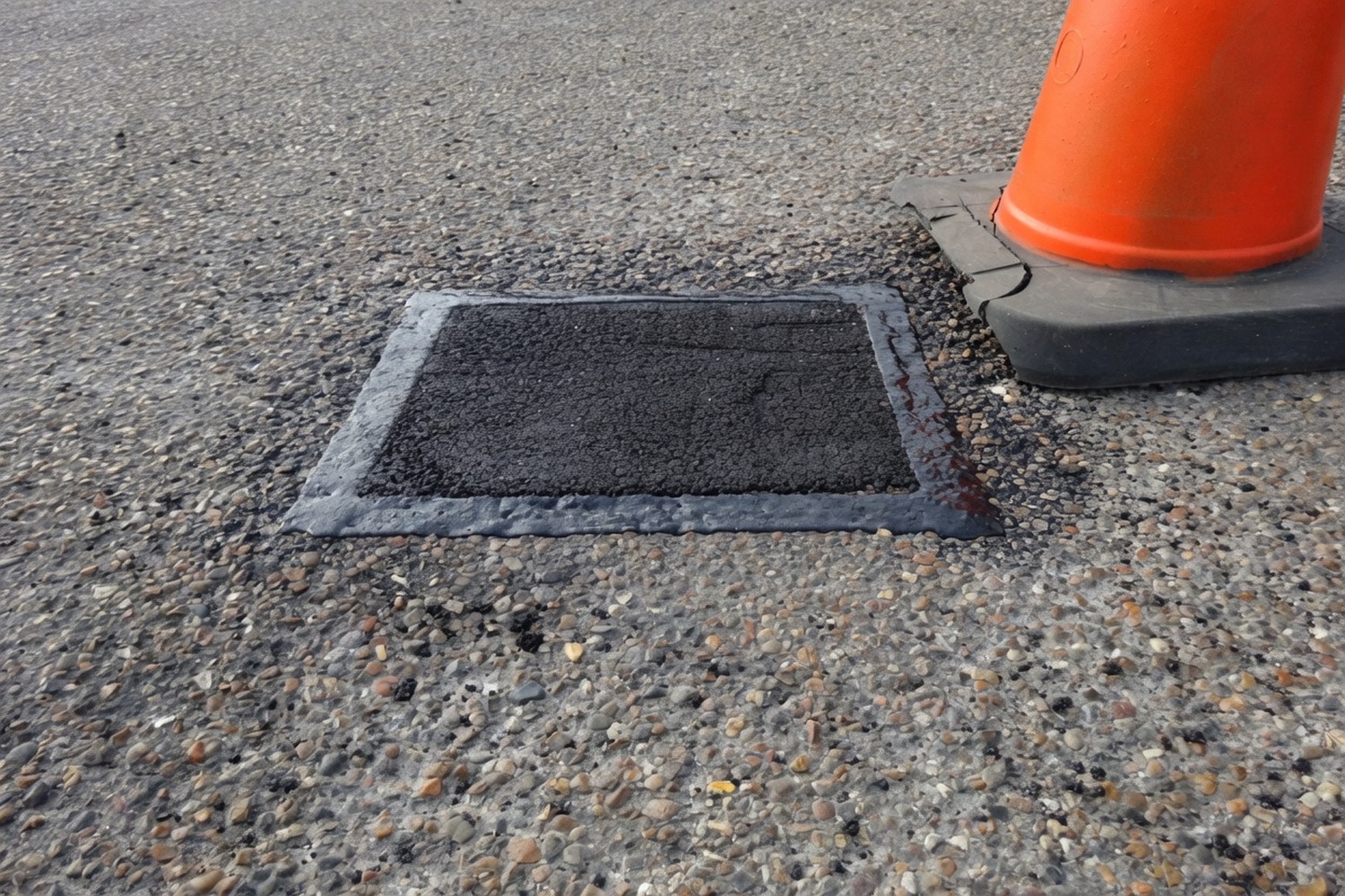 Fresh hot-mix asphalt patch with traffic cone in place during make-safe