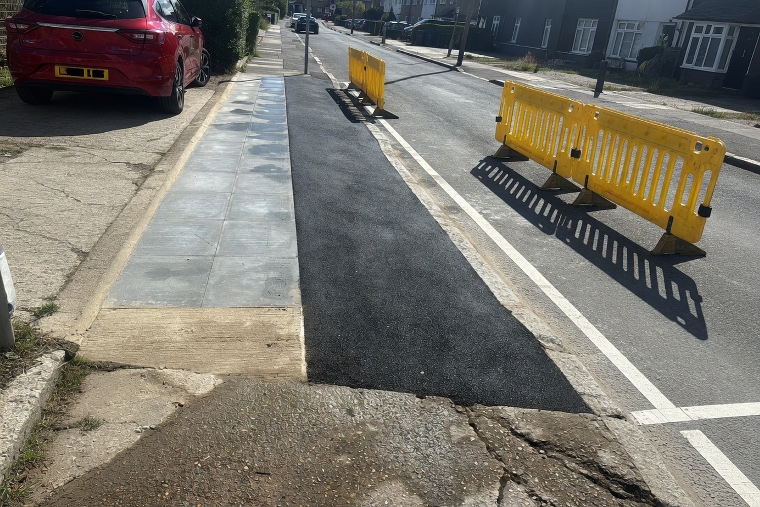 Footway asphalt repair beside a kerb with parked car