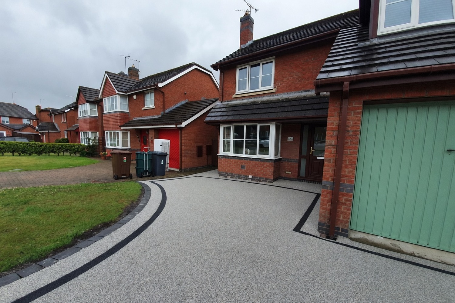 Red shingle driveway leading to a green garage door